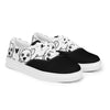 A pair of Orca Snork "Goofy Pup" women's canvas sneakers are shown from a slightly angled front view. The shoes feature a black and white print of goofy dog faces and hand-drawn hearts with a solid black toe cap.
