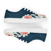 A single women's Orca Snork canvas sneaker is shown from a side view, with a second identical shoe positioned directly beneath it in an inverted, mirrored reflection. The sneaker has a dark navy blue upper and a cream-colored lower section with a pink and blue floral pattern. The shoes are set against a white background, highlighting the contrast of the white laces and soles.