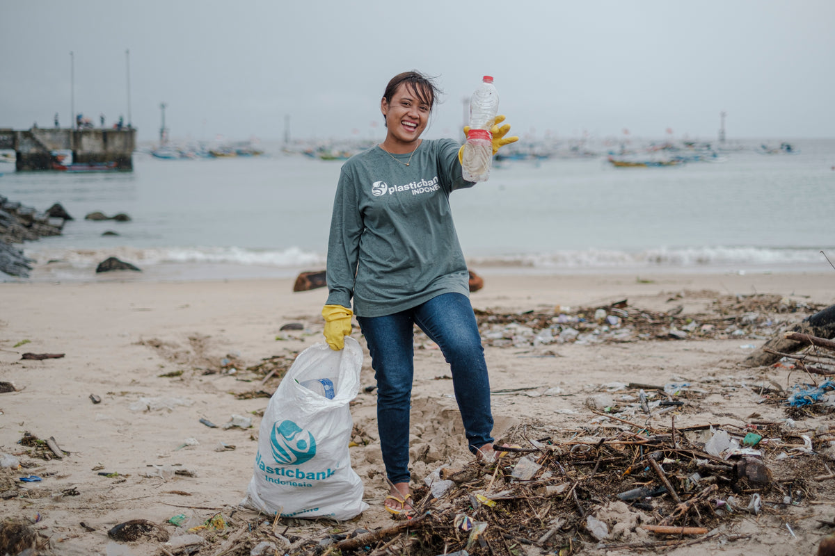 Plastic Bank Indonesia member holding collected plastic waste on a beach in Bali during a coastal cleanup.